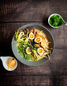 Schüssel mit Ramen von oben. Daneben ein Schälchen mit Chili und ein Schälchen mit gehckten Frühlingszwiebeln